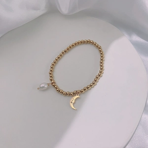Close-up of gold beaded bracelet featuring a pearl drop and crescent moon charm details