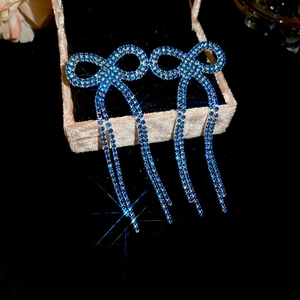 Macro detail of blue crystal bow tassel earrings resting in a pink velvet jewelry box