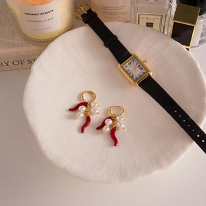 Dettaglio di orecchini d'oro con peperoncino rosso e perle su piatto di ceramica bianca