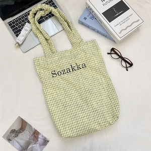 Top view of yellow plaid canvas tote with ruffled handles and a brand logo on front