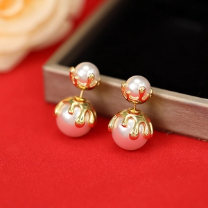 Macro view of double pearl drop earrings with golden dripping metal detail on red velvet