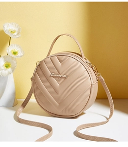 Detail of beige round crossbody bag featuring V-shaped quilting and gold metal logo
