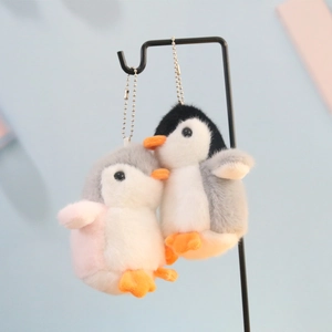 Close-up of cute plush penguin keychains with metal ball chains on a pastel background
