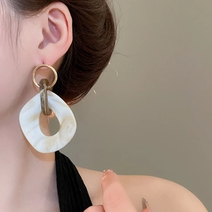 Close-up of irregular gold earrings with marble resin pendants worn on ear