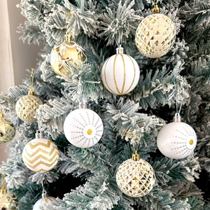 Detail of white and gold Christmas baubles with varied textures on snowy pine branches