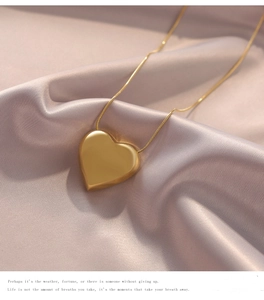 Macro shot of 3D gold heart pendant on a snake chain over soft silk background