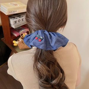 Detailed view of denim scrunchie with embroidered cherries on a high ponytail