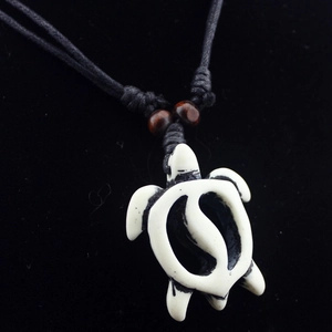 Retro turtle pendant necklace with bone-like carving and black cord on dark background