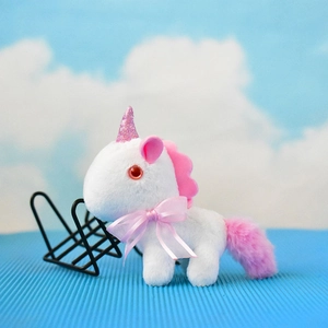 Nahaufnahme eines weißen Plüsch-Einhorn-Schlüsselanhängers mit rosa Schleife und Glitzerhorn.