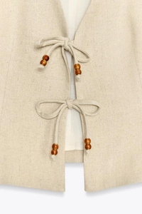 Detailed macro view of beige linen vest featuring front ties and brown wooden beads decoration