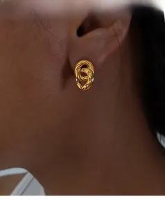 Close-up of woman wearing interlocking gold double hoop earrings with white zircon accents