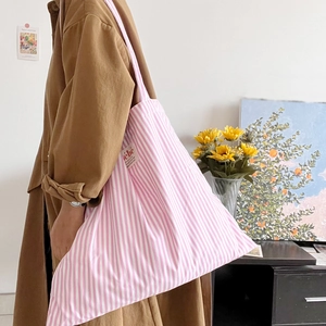 Dettaglio della borsa tote in tela a righe rosa indossata con un trench casual