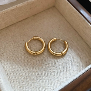 Close-up of polished gold round earrings on beige linen lining in a jewelry gift box