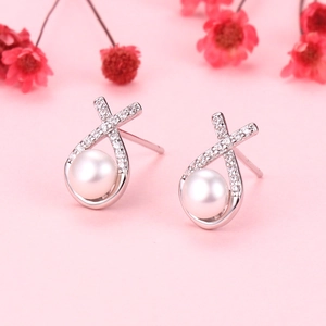 Crossed silver earrings with micro zircons and freshwater pearls on a pink background