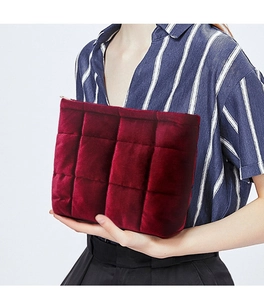 Close-up of a burgundy quilted velvet makeup bag held by a person on a white background