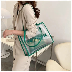 Close-up of a stylish transparent PVC tote bag with green leather trim and FASHION text