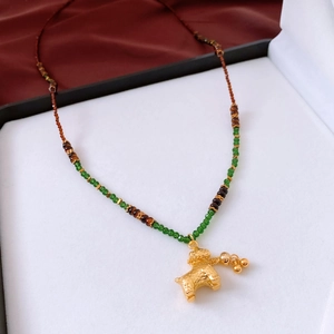 Detail of golden dog zodiac pendant with textured finish on colorful beaded chain