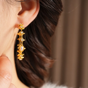 Detailed close-up of gold starburst hoop earrings with white pearls and zircons on model