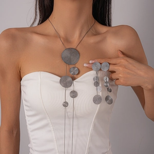 Detailed view of long silver tassel necklace and round textured earrings on a model