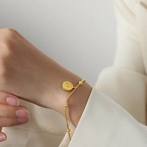 Retro gold-plated chain bracelet with a coin-style pendant and beads on a female wrist