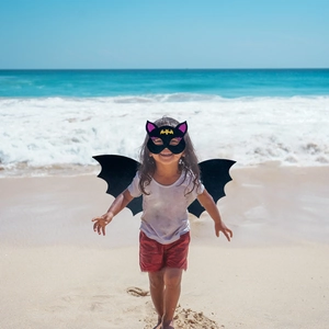 Black bat wings and mask costume set for kids shown on a beach setting outdoors
