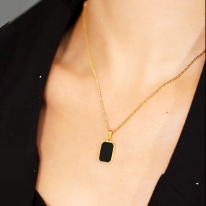 Close-up of golden titanium necklace with square black pendant worn on neck