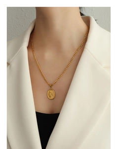 Détail d'un collier doré avec pendentif ovale orné d'un motif floral en relief sur mannequin