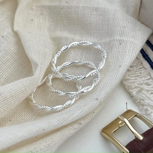 Close-up of three stacked 925 sterling silver twisted rope rings on a beige linen surface
