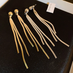 Detail of long snake chain tassel earrings in gold and silver finish on black fabric