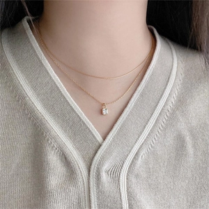 Detail of a layered gold bamboo chain necklace with a sparkling square zircon lock pendant