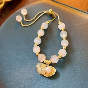 Detail of pink cat-eye bead bracelet with gold shell pendant and white pearl charm