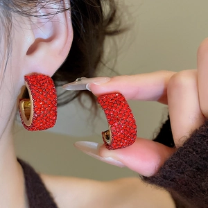 Detailed close-up of red rhinestone encrusted C-shaped hoop earrings with gold base