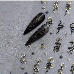 Macro detail of metallic gold snake and star moon nail art stickers on black long nails