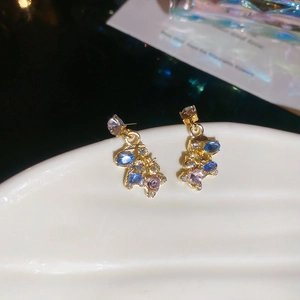 Macro shot of gold earrings featuring blue and pink crystals on a white shell tray