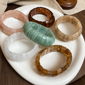 Detailed close-up of six multicolor resin elastic bracelets arranged on a ceramic dish