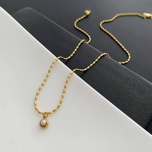 Minimalist gold titanium necklace with pearl pendant on a modern bicolored background