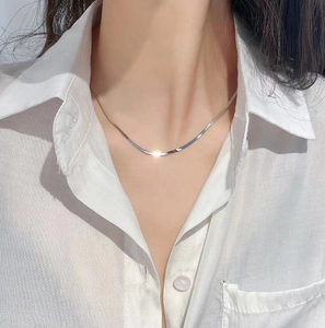 Detailed view of layered silver snake bone chains on a white shirt worn by a female model