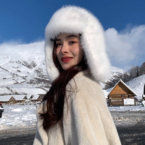 Detail of white faux fur winter earflap hat and plush coat against a snowy mountain scene