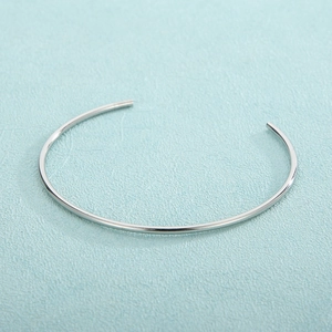Polished silver minimalist open bangle shown on a light blue textured surface