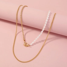 Close-up of layered gold rope chain and white pearl necklace with metallic OT toggle clasp