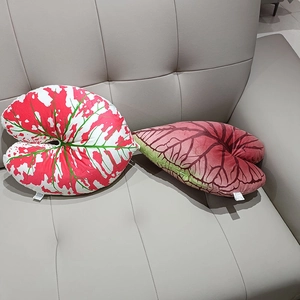 Detail of red and pink leaf-shaped plush pillows displayed on a grey leather sofa