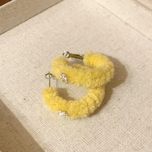 Detail of yellow flocked hoop earring with silver floral accents on a beige fabric box
