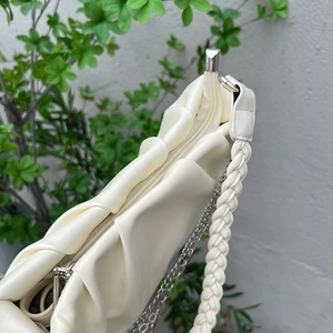 Close-up of beige cloud bag featuring ruched pleats, woven strap and silver metal chain