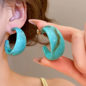 Detailed view of large C-shaped acrylic earrings with green marble texture worn on ear