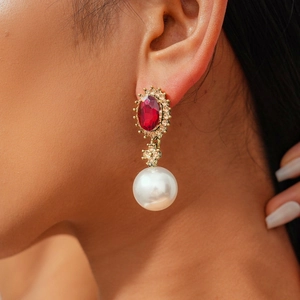 Close-up of vintage drop earrings featuring a red oval gemstone and white pearl