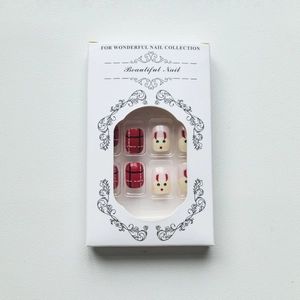 Macro view of Christmas press-on nails with red plaid and reindeer patterns in box