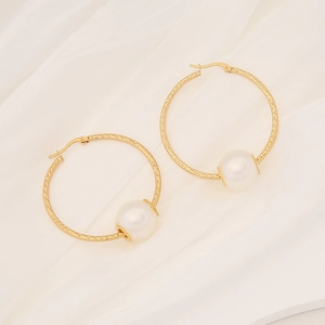 Detail of textured gold hoop earrings with white pearl accent on draped fabric