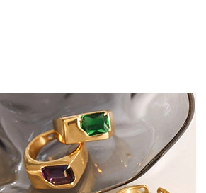Macro shot of 18K gold rings featuring large emerald green and purple gemstones
