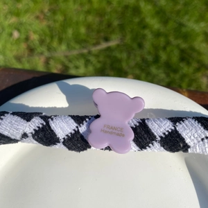 Détail d'une pince à cheveux ours lavande avec motif à carreaux noirs et blancs sur herbe