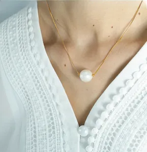 Close-up of golden snake chain necklace with a single white pearl on a model neckline